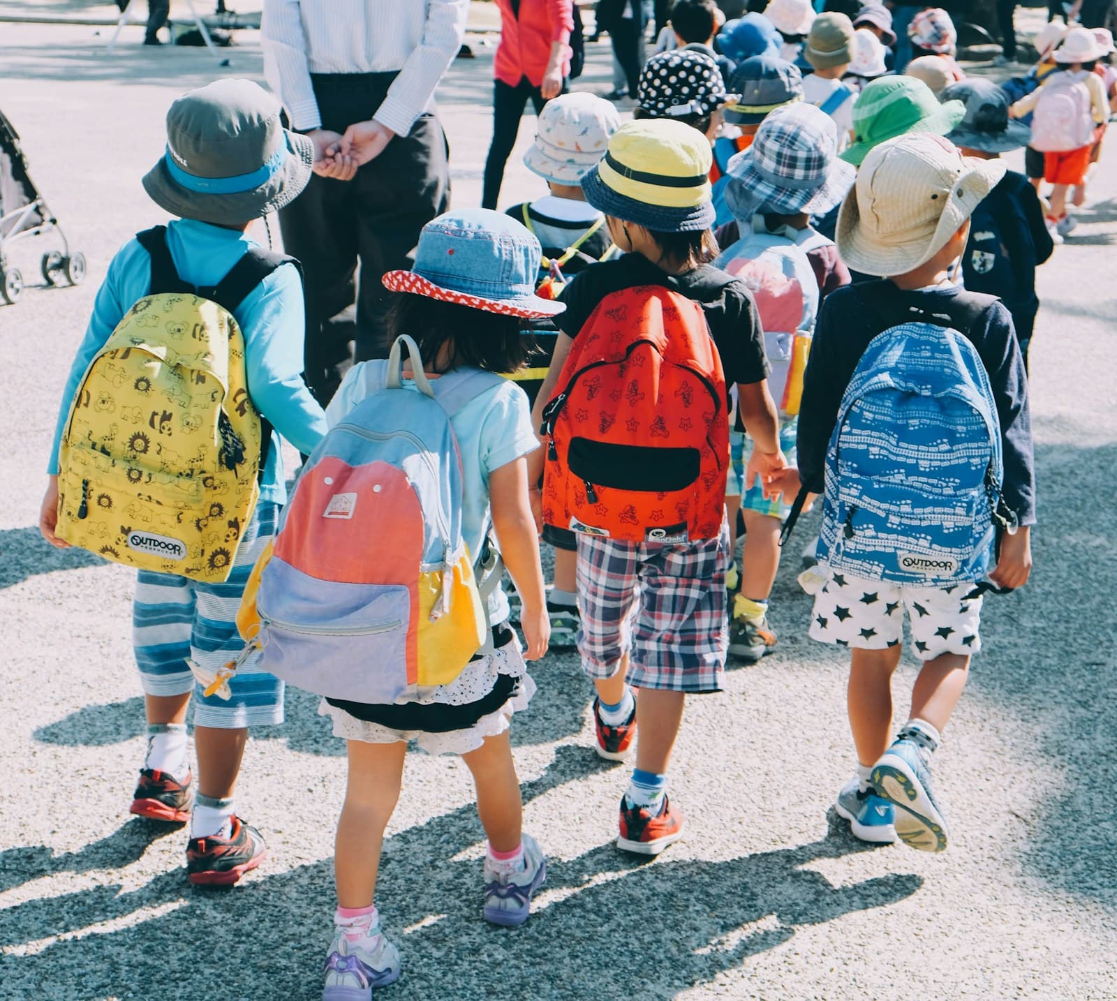 Un groupe d'élèves marche sur un trottoir, sacs à dos clairs sur le dos.