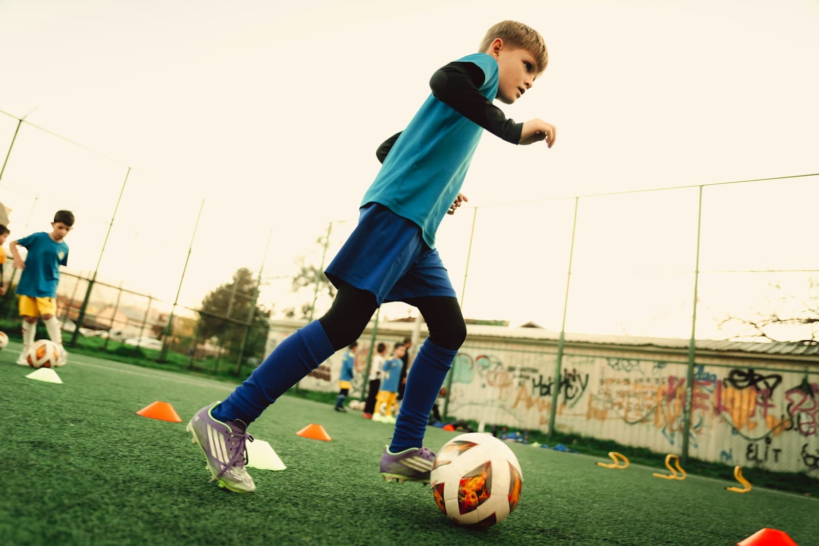 Un garçon conduit un ballon de football sur un terrain.