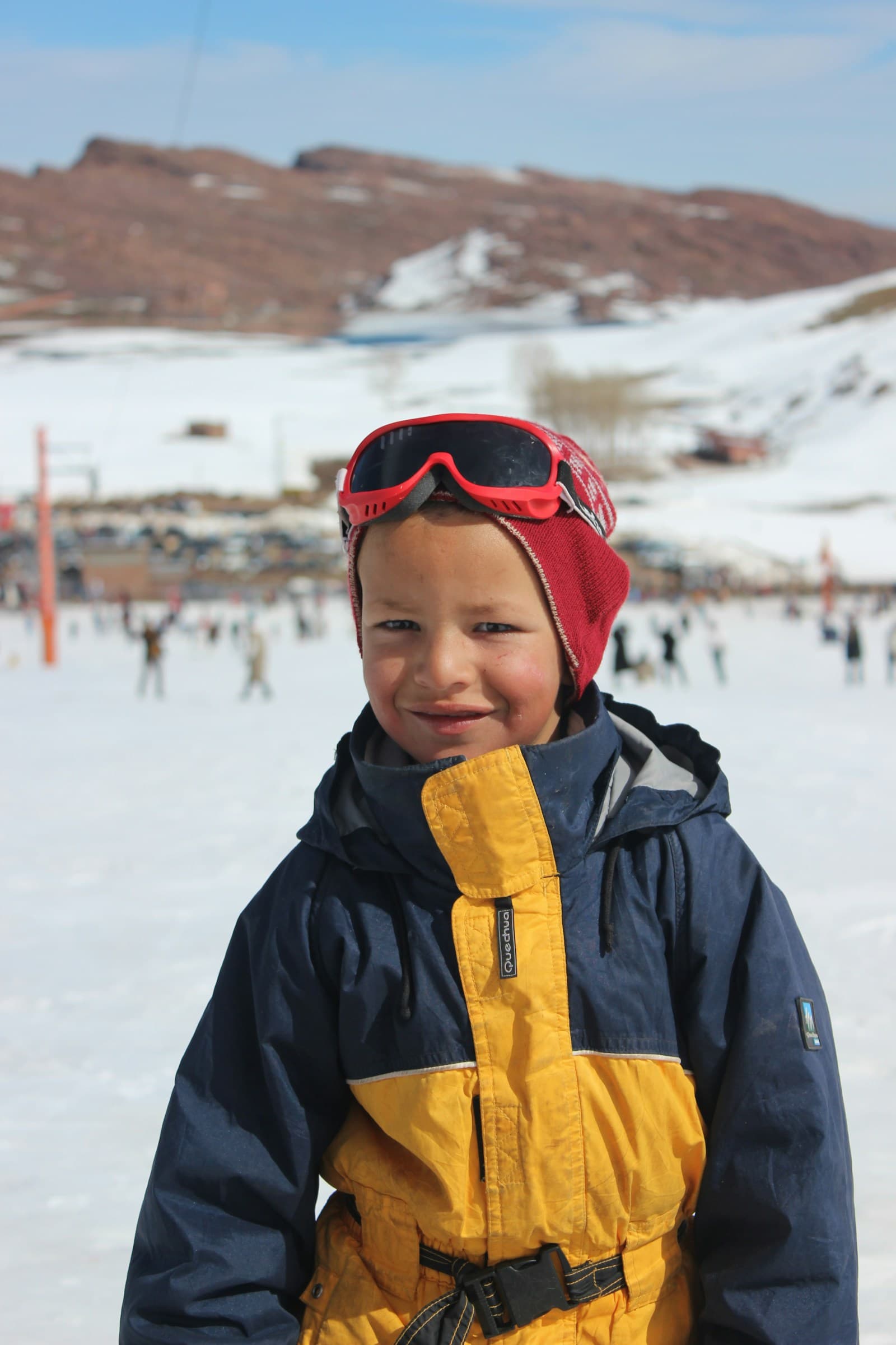 Un garçon en tenue de ski sourit, masque relevé sur le bonnet.
