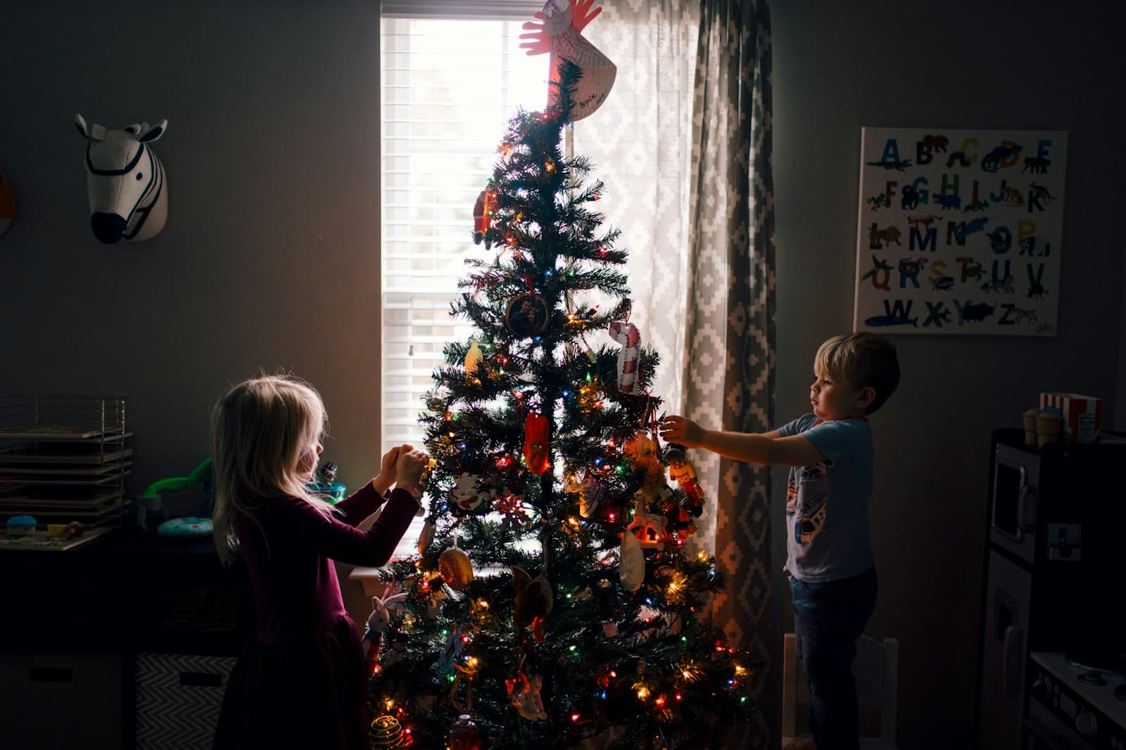 Une fille et un garçon debout devant un sapin illuminé.