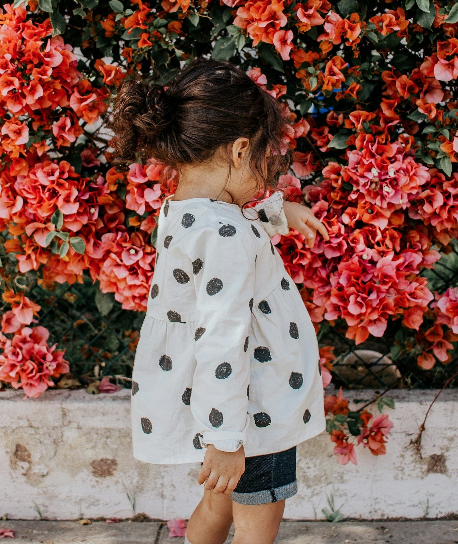 Une fille en blouse à pois et short bleu, à côté de fleurs rouges.
