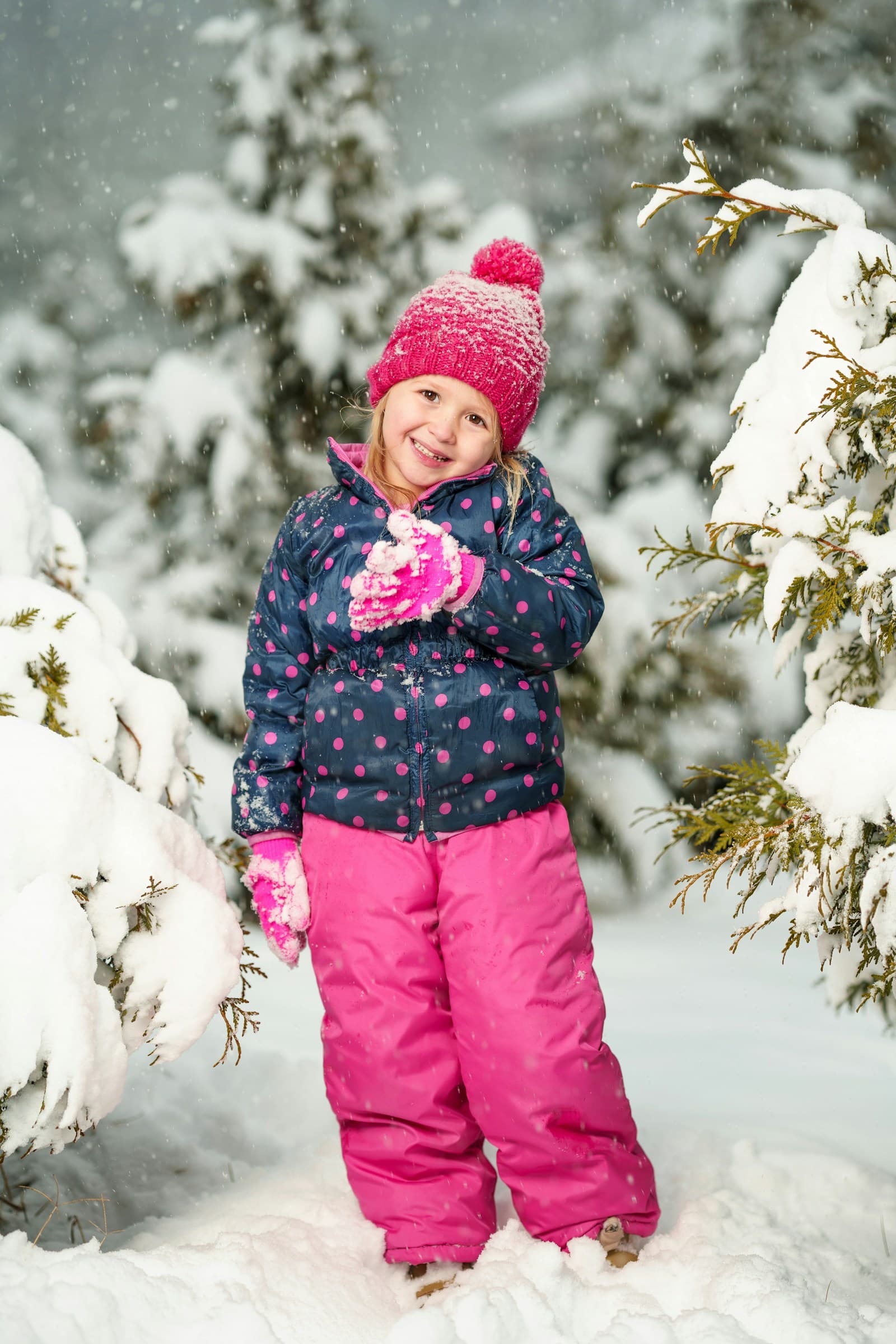 Une fille sourit dans la neige, devant des arbres enneigés.
