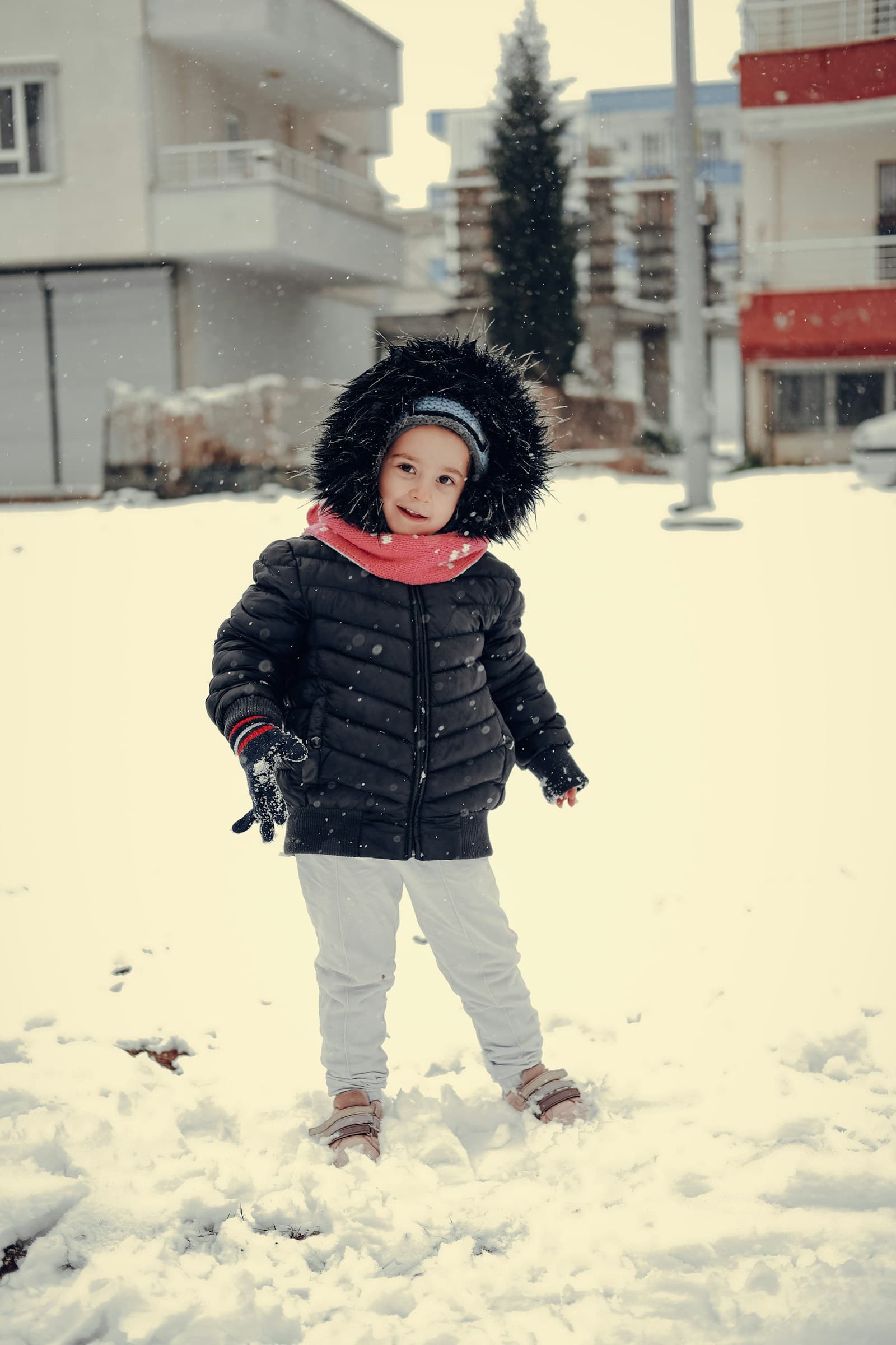Une petite fille debout dans la neige, coiffée d'un chapeau en fourrure.