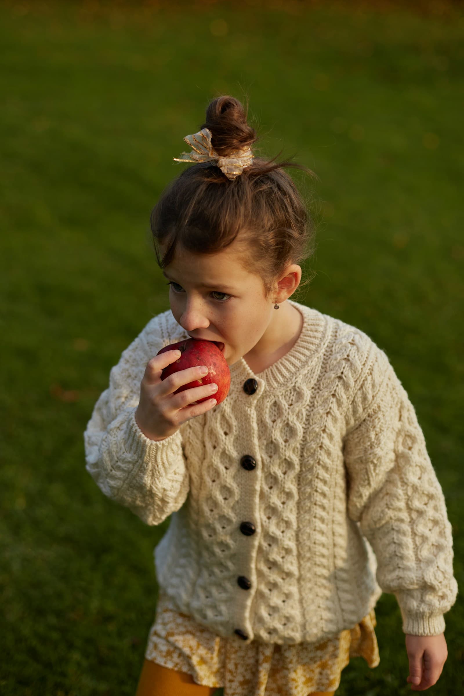 Une fille croque une pomme, debout dans un champ.