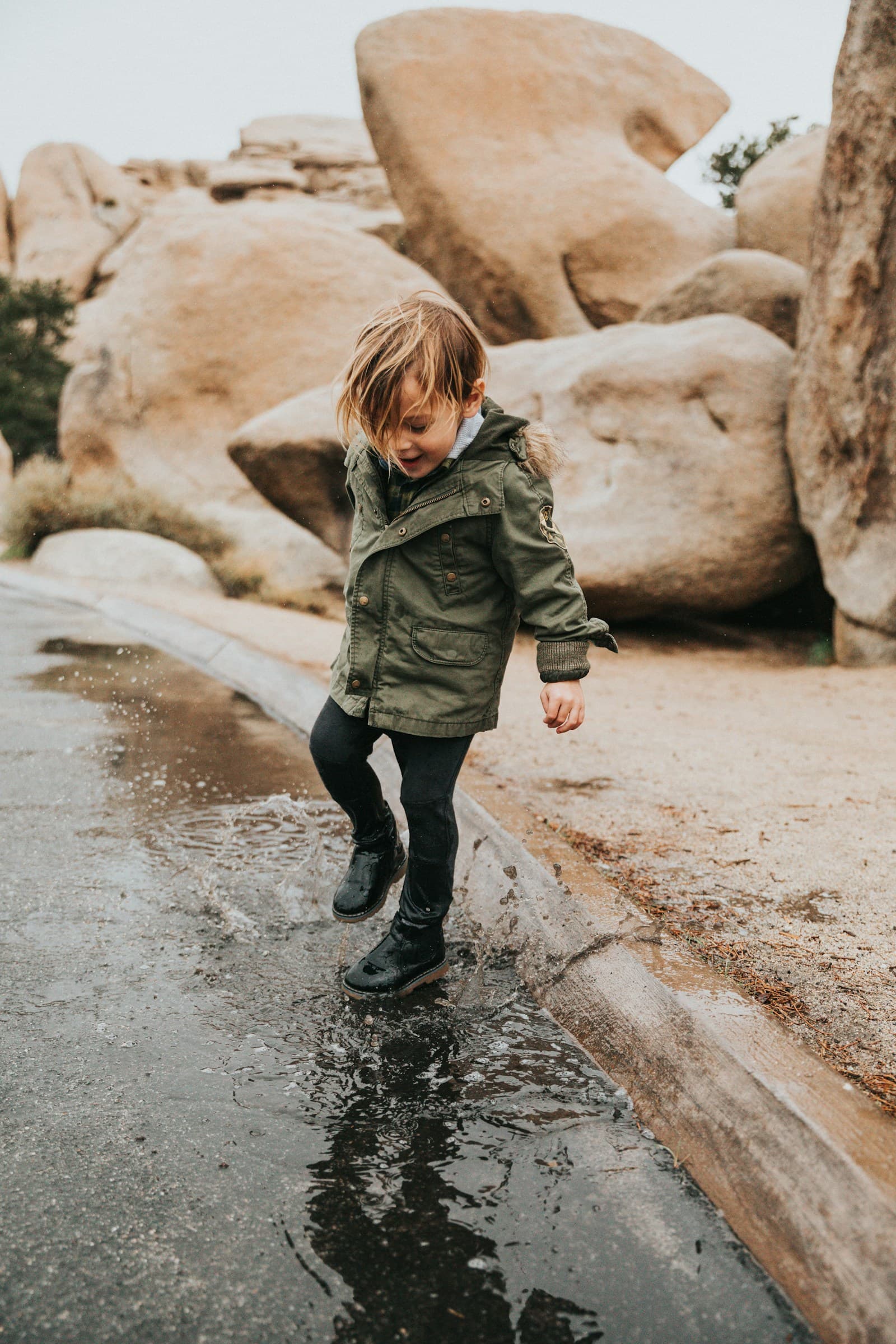 Une fille en veste verte et pantalon foncé marche sous la pluie.