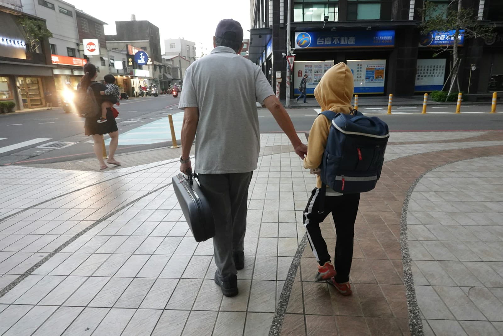 Un adulte et un enfant marchent main dans la main sur un trottoir.
