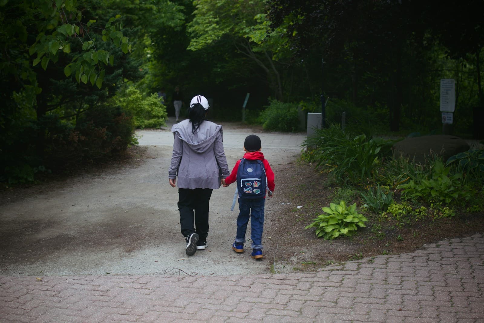 Une femme et un enfant marchent main dans la main sur une allée de parc.